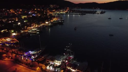 Aerial shot of port during night time with boats docked. Many street lights. Revealing sunset colors