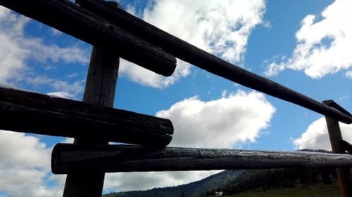 Time lapse focused on a wooden fence. Clouds are seen going by with a green meadow in the background