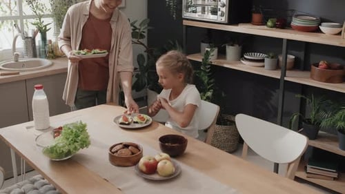 Child Eating Sandwich with Mother in Kitchen