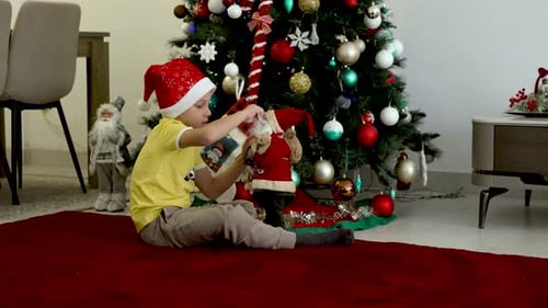 Boy Plays with Christmas Presents by Decorated Tree