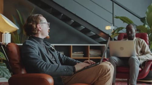 Two Businessmen Using Laptops and Having Discussion in Comfortable Office