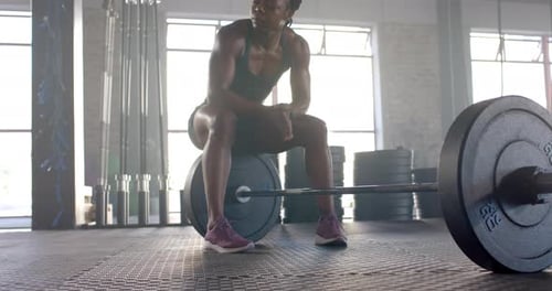 Resting on barbell, woman in gym taking break from weightlifting workout