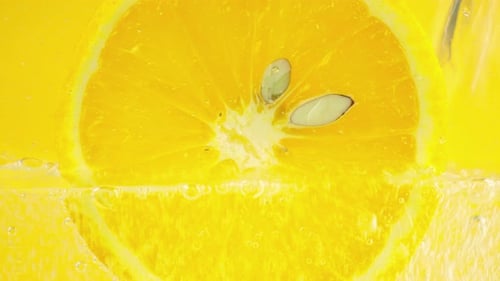 A slice of ripe orange in water bubbles on an orange background.