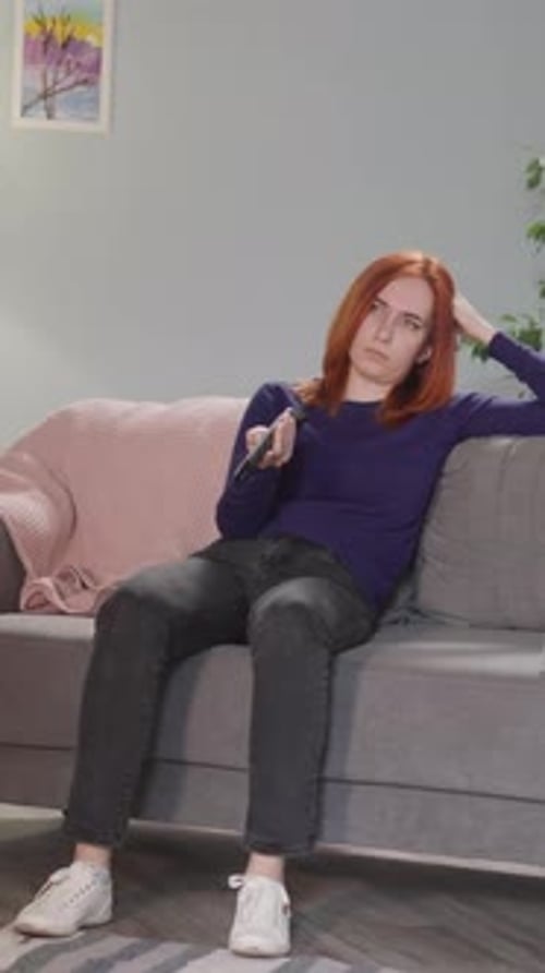 Tired Redhead Woman Changes TV Channels Using Remote Control
