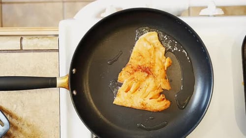 Placing a seasoned salmon fillet in a frying pan with hot oil for a tasty meal - overhead view