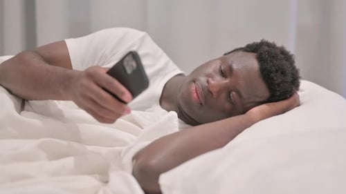 Young Adult Lying in Bed Looking at Phone