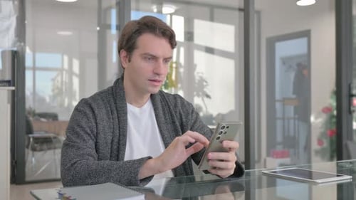 Young Man Celebrating Success on Phone in Office