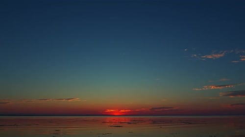 Meditative Aufnahme, türkisroter und rosafarbener Sonnenuntergang, Sonne und Wolken, die sich im Wasser spiegeln, die Sonne verschwindet