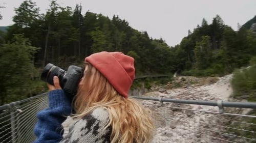 Woman With Camera Walks on Suspension Bridge in Mountains