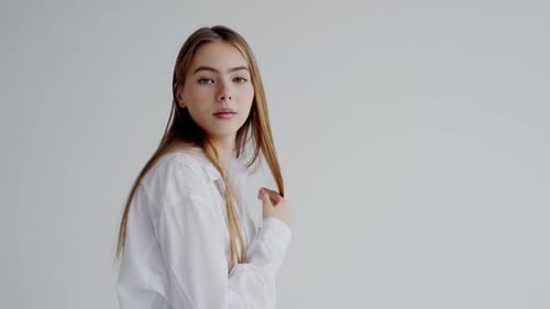 Young Woman in White Shirt Smiling Against Plain Background