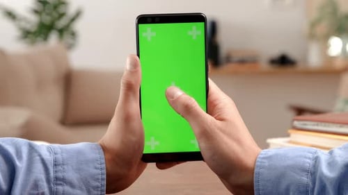 Man taps green screen smartphone for video call in home office mockup