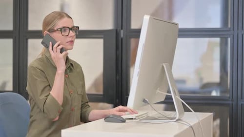 Woman Talking on Smartphone at Computer Workstation