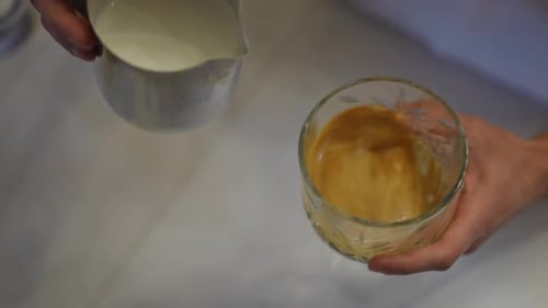 Closeup Pouring White Milk in Glass with Black Coffee in Slow Motion Closeup High Angle View