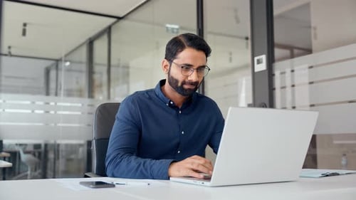 Smiling Indian Business Man Looking at Laptop Using Computer Working in Office