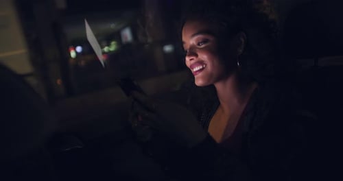 A young woman using a smartphone in a car in the city at night
