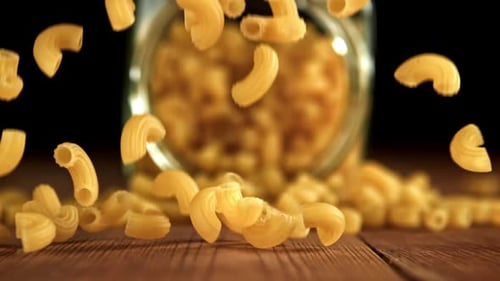 Elbow macaroni falling onto a wood table