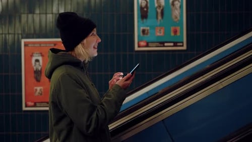 A nice lady is smiling while responding to a message on her phone while taking the escalator stairs