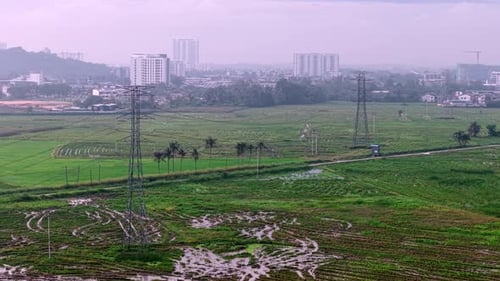 Aerial electric pole transmission towers over wet rice fields and city
