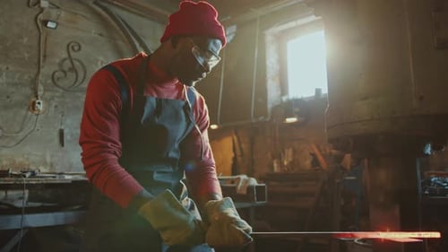 African American Blacksmith Forging Iron Billet with Press Machine in Workshop