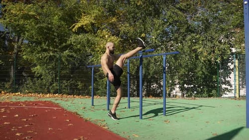 A Man Stretches His Legs at the Horizontal Bars Outdoors
