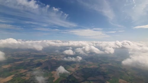 slow flying with an airplane trough the clouds and flat farm land of Germany visible bellow