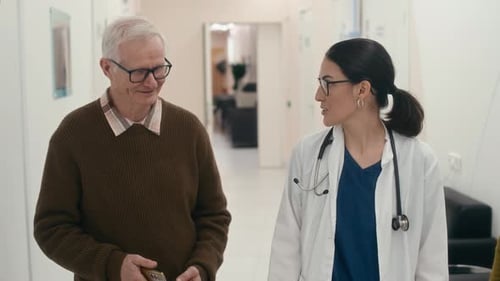 Physician Consulting Senior Patient Walking along Clinic Corridor