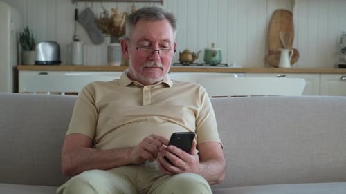 Senior Man Using Smartphone on Couch at Home