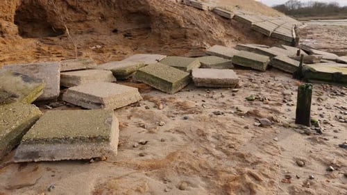 Broken tiles scattered across beach from damaged sea wall. Due to the decay in management the powerf