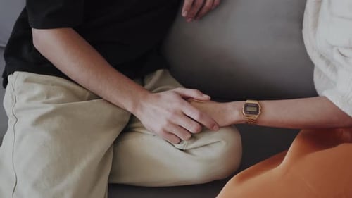 A Closeup Image Capturing Two Individuals Holding Hands While Seated on a Couch