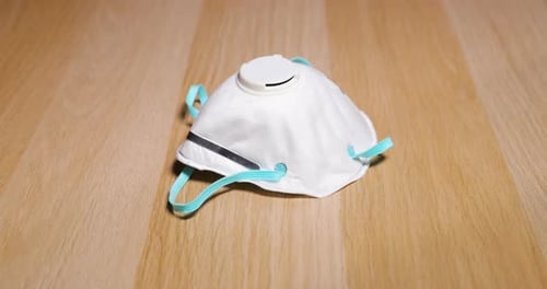 Hand Picks Up White Face Mask from Wood Surface