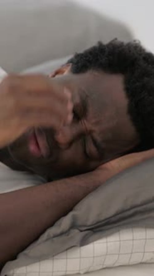 Vertikales Video eines afrikanischen Mannes mit Kopfschmerzen, der auf der Seite im Bett liegt