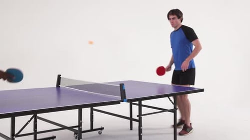 Playing table tennis, man hitting ball with paddle in studio setting