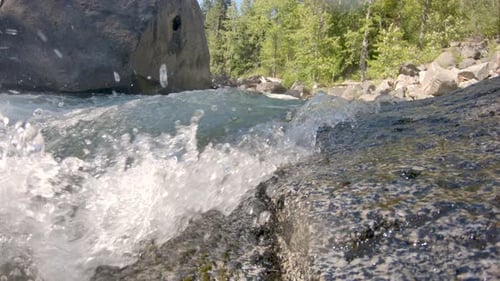 Low angle view of river water rushing over rock. Water splashes camera. Static shot.