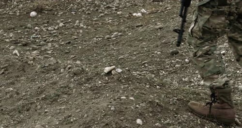 Soldier in Camouflage Walking Across Rocky Terrain