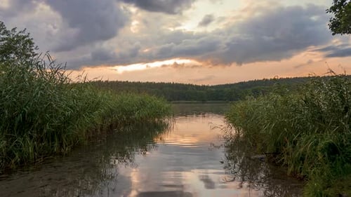 time lapse at a small forest lake with the setting sun and passing clouds