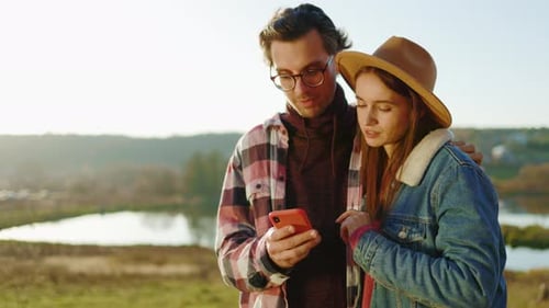 Close Up Young Lovely Couple Man and Woman Use Phone in the Forest Near Lake Feel Happy Smiling