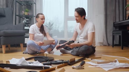 A married couple independently assembles new furniture from a set of parts.