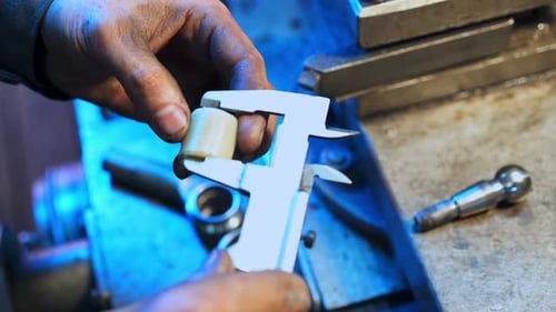 Dirty hands of a turner measuring the plastic piece with the help of calipers.