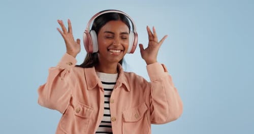 Happy woman, headphones and dancing to music, audio or sound track against a studio blue background