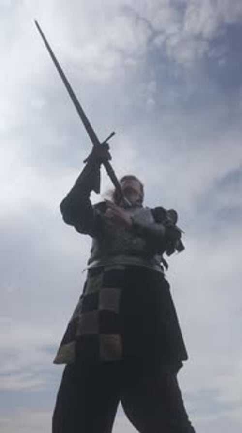 Man in Medieval Armor Holds Sword Upright