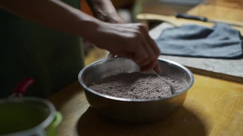 Mischung aus Pulver und weißer Blume wird mit einem Löffel in einer Schüssel auf der Küchentheke gerührt, gefilmt als cl