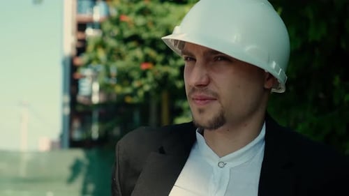 Ein professioneller Baumeister mit KN 95-Maske und Schutzhelm auf einer Baustelle spricht mit einem Mitarbeiter