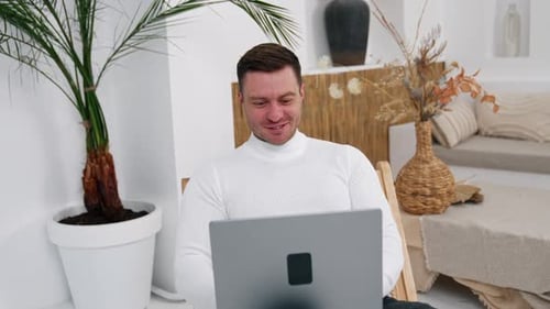 Young male in good humor sitting in front of the computer. Man works at home freelancing.