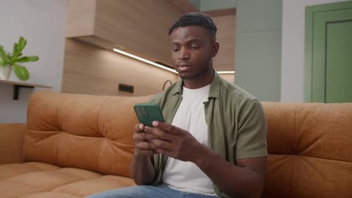 Black Man Typing on Phone Sitting on Couch 20s African American Male is Smartphone Addicted at Home