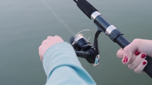 Hände einer Fischerin mit einer Spinnrute in einer Nahaufnahme einer Hand. Drehung des Griffs mit