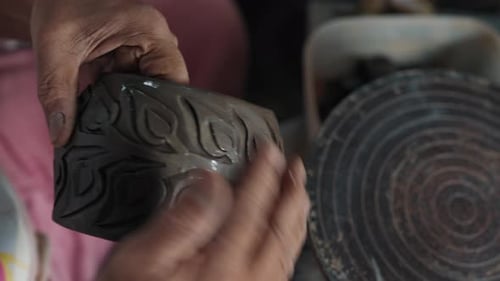 Hands crafting clay vase with engraved design