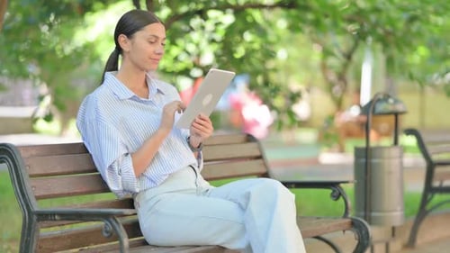 Woman Uses Tablet on Park Bench on Sunny Day