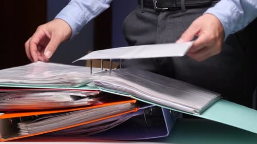 Person Organizing Documents in Office Binder Searching Paperwork