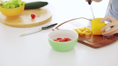 Woman cutting yellow pepper on cutting board