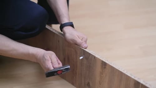 Man Assembling Furniture Inserts Pegs with Hammer